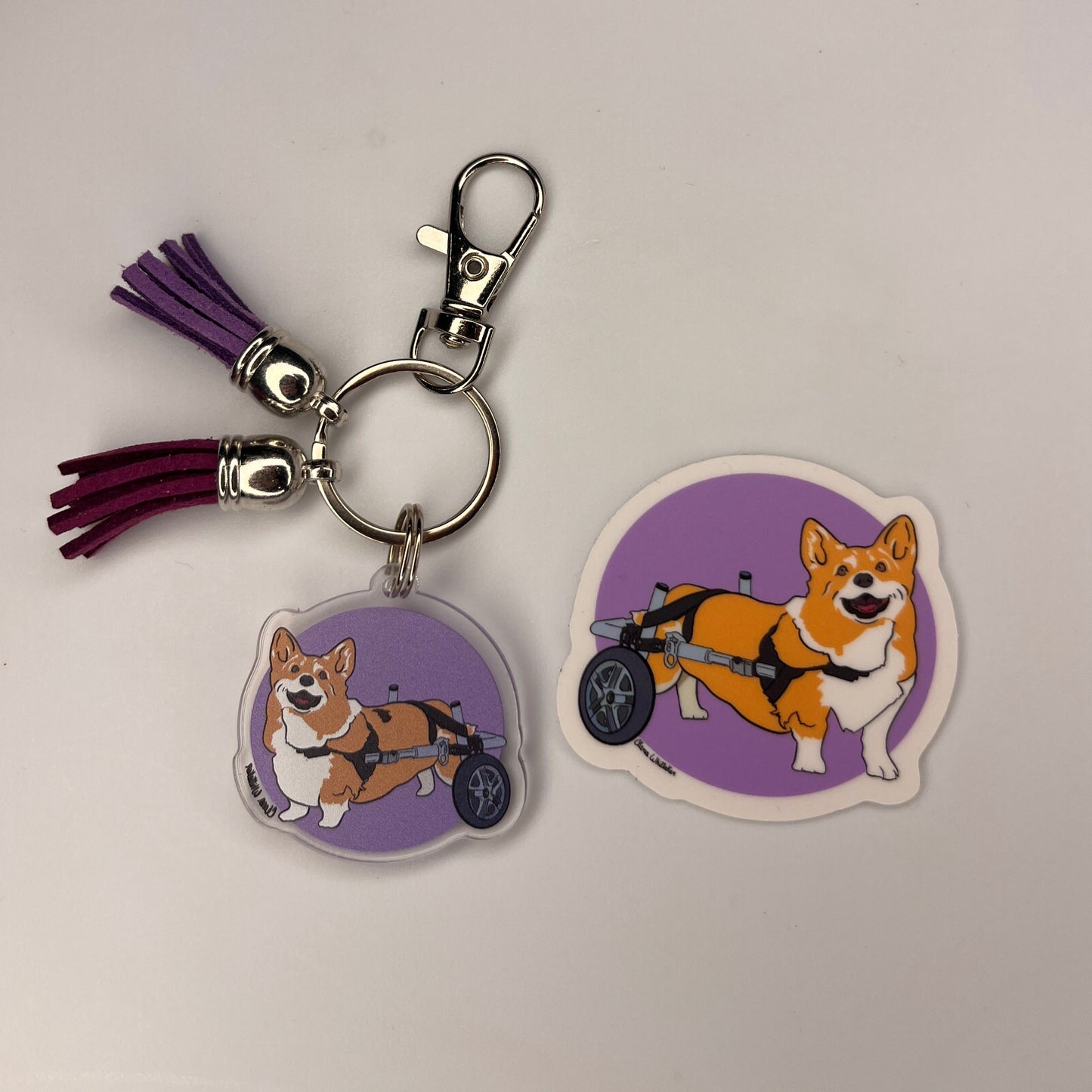 Corgi charm with two tassels metal lobster clasp and keyring next to a 2" x 2" vinyl Corgi sticker on a purple background