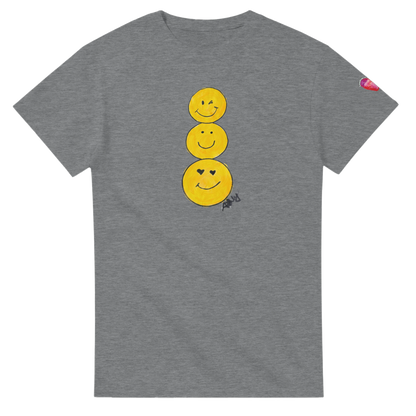 A heather gray short-sleeve T-shirt featuring a graphic of three stacked yellow smiley faces on the front, by Ashley Caldwell with a small pink heart patch on the left sleeve.